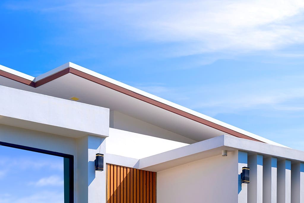 A modern house with a flat roof, white walls, vertical slats, and wood paneling, set against a bright blue sky with clouds.