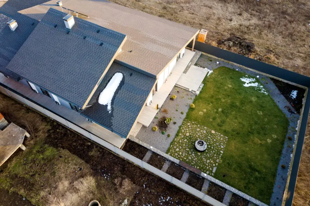 Aerial view of a residential home with dark asphalt shingle roofing and patches of melting snow.