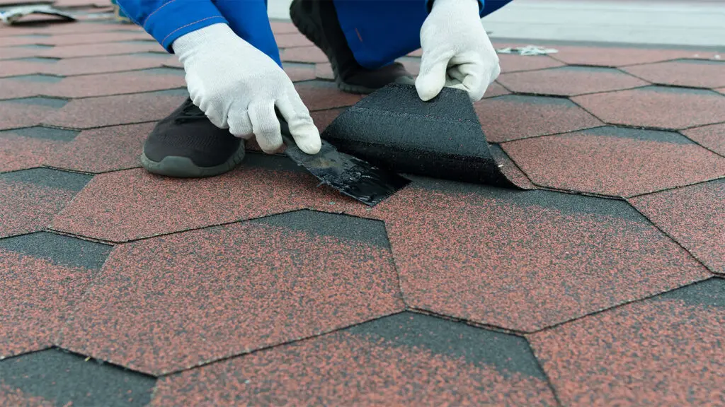 Roofer applying black mastic to a loose shingle during a roof maintenance visit in Forsyth, GA.