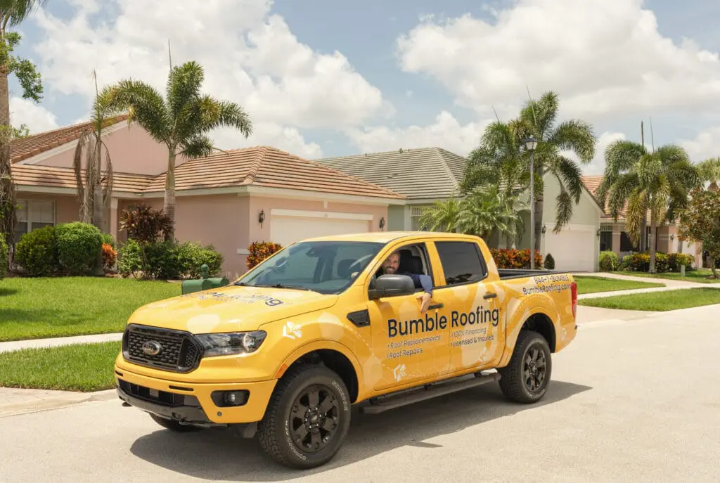 Yellow Bumble Roofing truck parked in front of suburban homes, promoting roof replacement and repair services under sunny skies