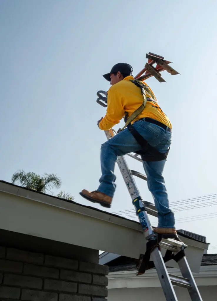 Bumble roofer stepping from a ladder to a roof carrying tools